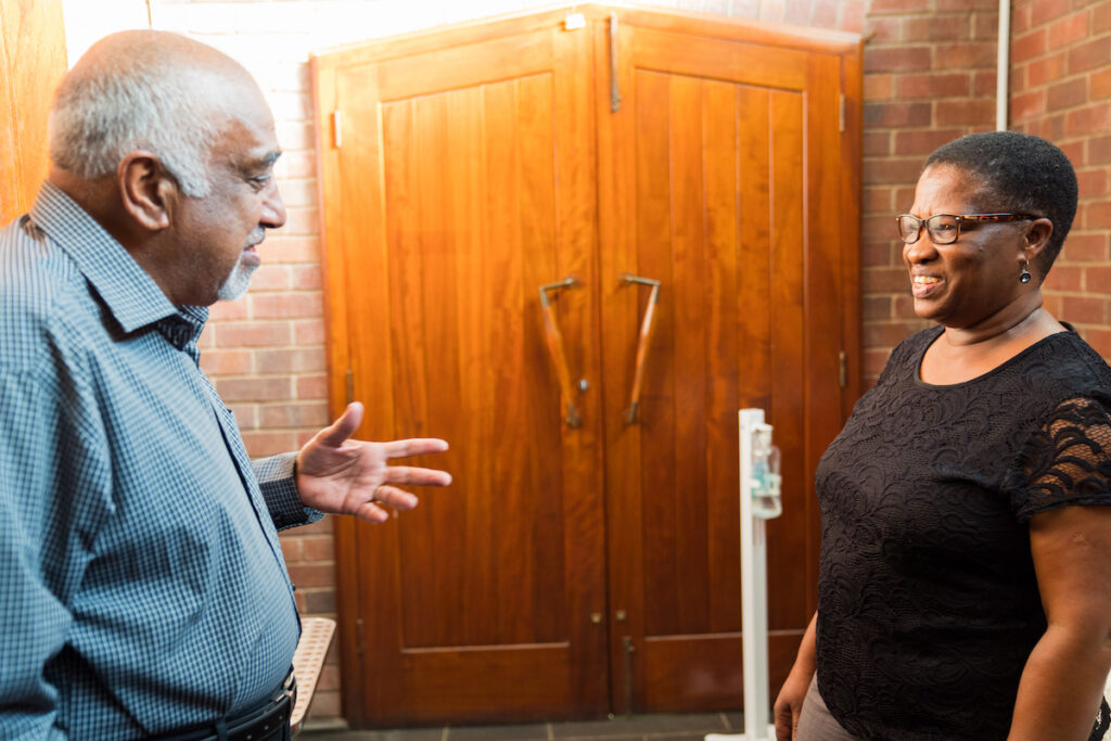 Kgabo Ledwaba is standing in a church, in front of two wooden doors, talking with one of her mentors.
