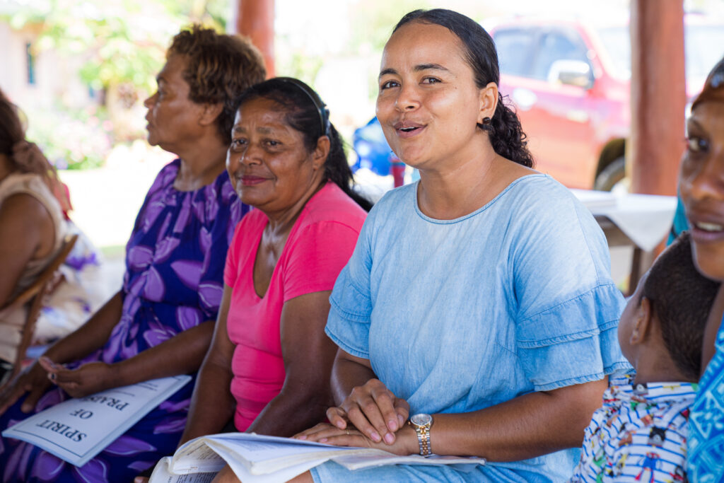 Four women sit on a bench singing during a worship service at a church in Fiji.