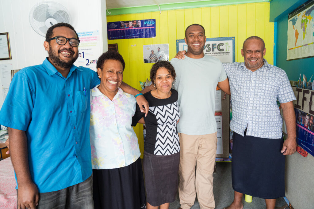A group of college ministry leaders in Fiji stand together smiling in their office.